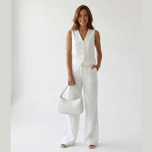 Woman wearing a white outfit holding a white handbag against a plain background