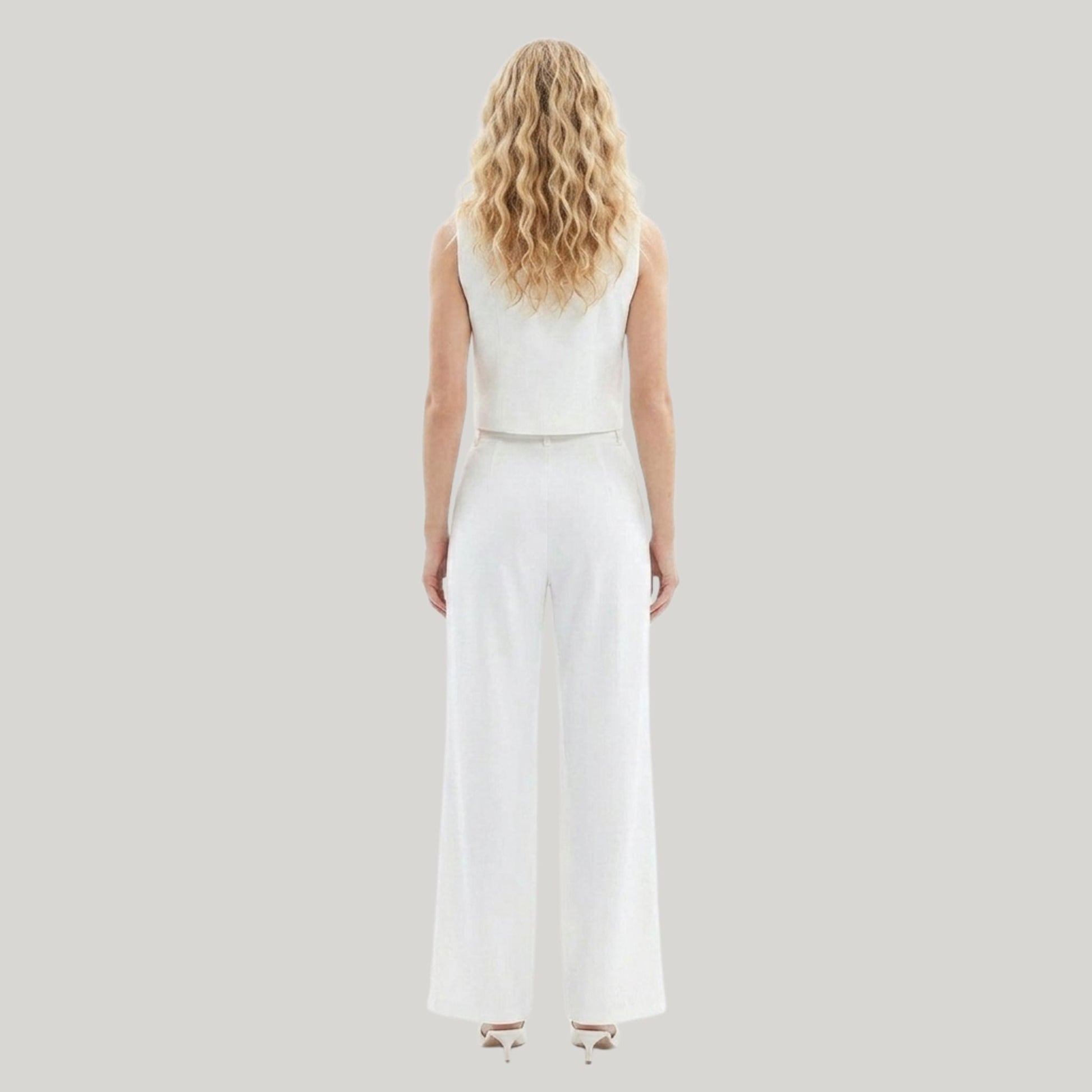 Woman wearing a white sleeveless top and wide-leg pants on a light gray background